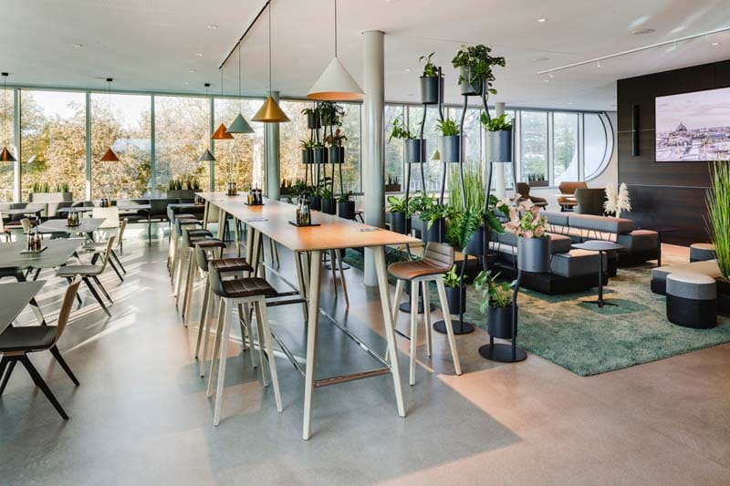 Cafeteria Einrichtung mit unterschiedlichen Sitzmöglichkeiten abgetrennt durch große Pflanzenfront