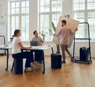 Drei Personen bei der Gruppenarbeit, eine Person trägt ein Whiteboard