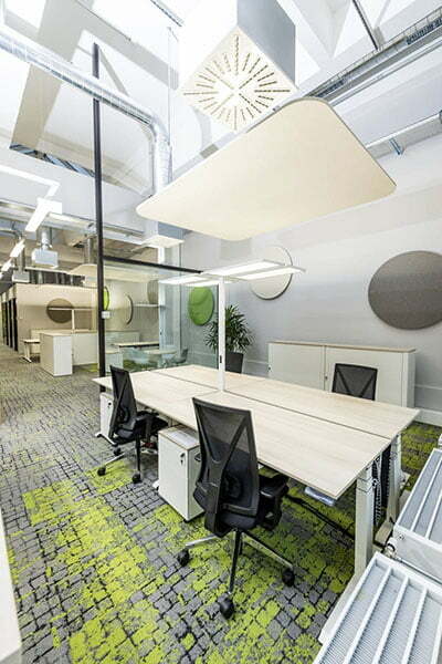 Vier Arbeitsplätze bestehend aus Schreibtischen und Bürostühlen, grün-grauer Teppichboden