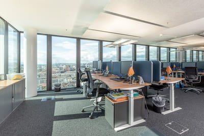 Open Space Büro ausgestattet mit Akustikelementen an den Schreibtischen vor großer Fensterfront mit grauem Teppichboden