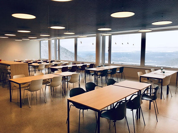 Cafeteriaeinrichtung mit vielen Tischen und Stühlen vor großer Fensterfront