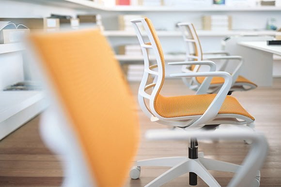 Drei orangene Bürostühle an Arbeitsplätzen stehen hintereinander