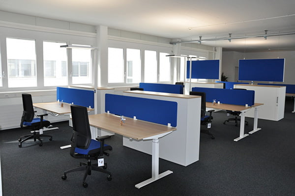 Mehrere Arbeitsplätze mit blauen Akustikwänden, die an den Schreibtischen befestigt sind